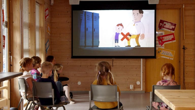 Barn i barnehagealder sitter på stoler og ser på en tegnefilm som vises på et prosjektorlærret. På filmen kan du se en gutt og en voksen mann. Mannen har åpnet buksesmekken og har en erigert penis. Over mannen og penisen er det et stort rødt kryss som viser at det ikke er greit.