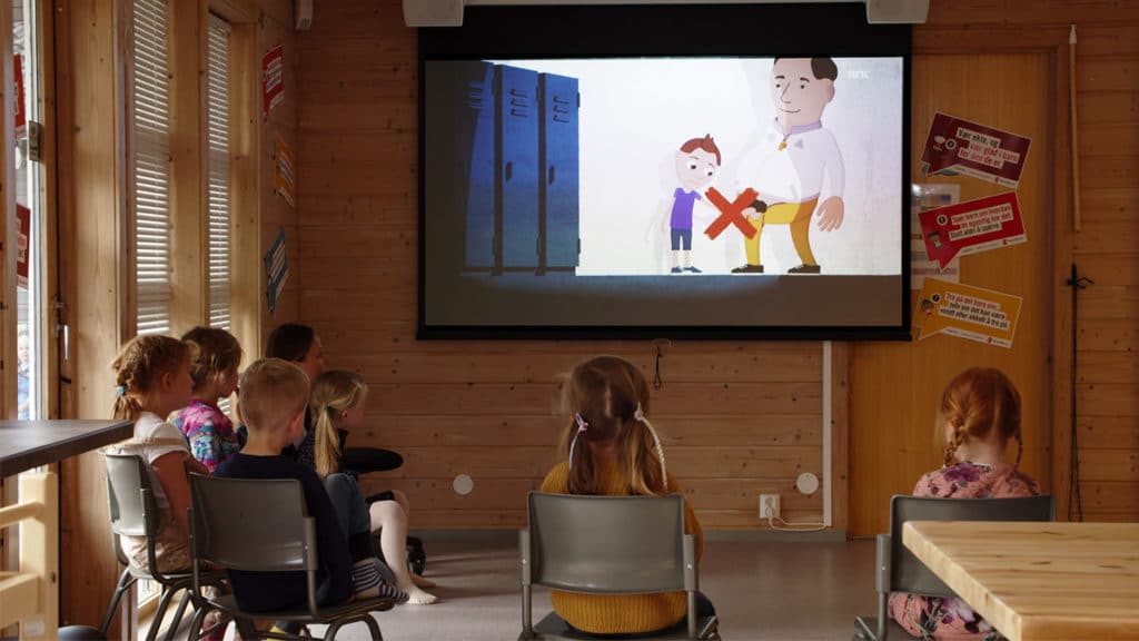 Barn i barnehagealder sitter på stoler og ser på en tegnefilm som vises på et prosjektorlærret. På filmen kan du se en gutt og en voksen mann. Mannen har åpnet buksesmekken og har en erigert penis. Over mannen og penisen er det et stort rødt kryss som viser at det ikke er greit.