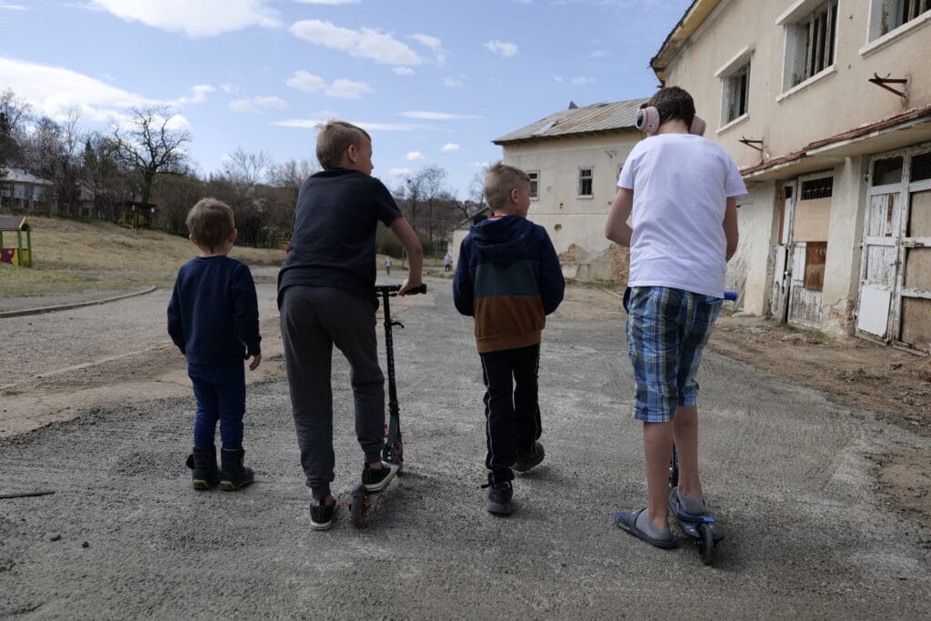 4 gutter med 2 sparkesykler står med ryggen til utenfor et dagsenter for barn på flukt fra Ukraina