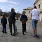 4 gutter med 2 sparkesykler står med ryggen til utenfor et dagsenter for barn på flukt fra Ukraina
