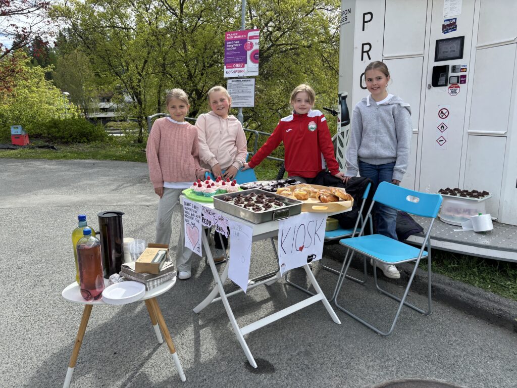 Fire jenter står foran et bord med kaker, smiler