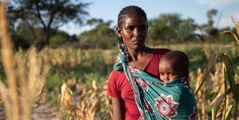 En mor står i en uttørket åker med barnet sitt i sjal. Altofr mange barn står overfor alvorlig matmangel og sult etter at El Niño-forårsakte tørkeperioder har ødelagt avlinger og tørket ut viktige vannkilder.