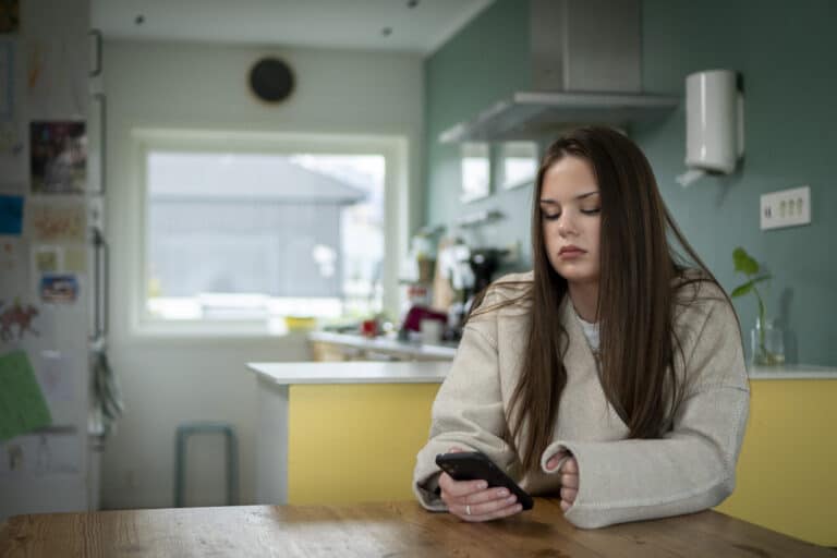 En ungdom sitter på mobiltelefonen sin på et kjøkken