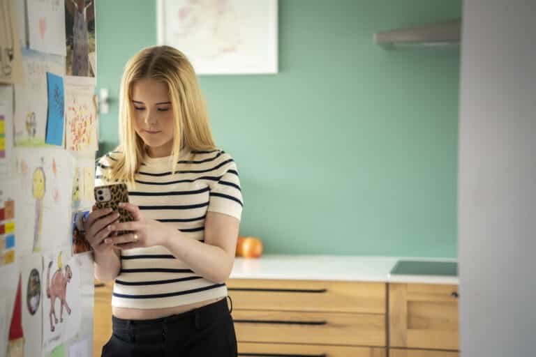 En ungdom står på et kjøkken, ser på mobiltelefonen