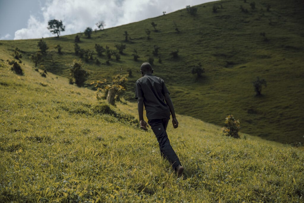 En tenåringsgutt ikledd militærgrønn går oppover grønne åser i Den demokratiske republikken Kongo