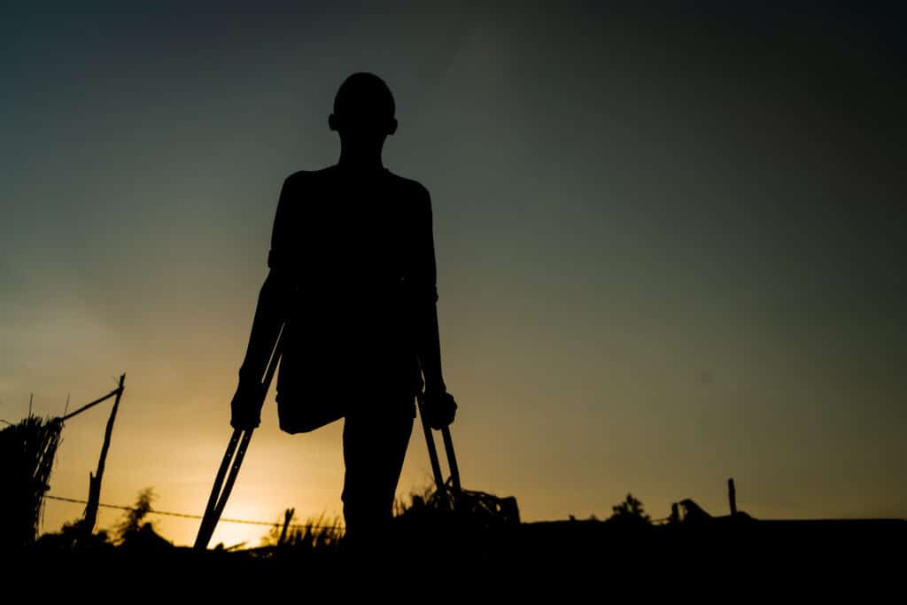 Skygen av gutt i solnedgang. Gutten går på krykker fordi han har mistet beinet da en bombe eksploderte nær hjemmet deres
