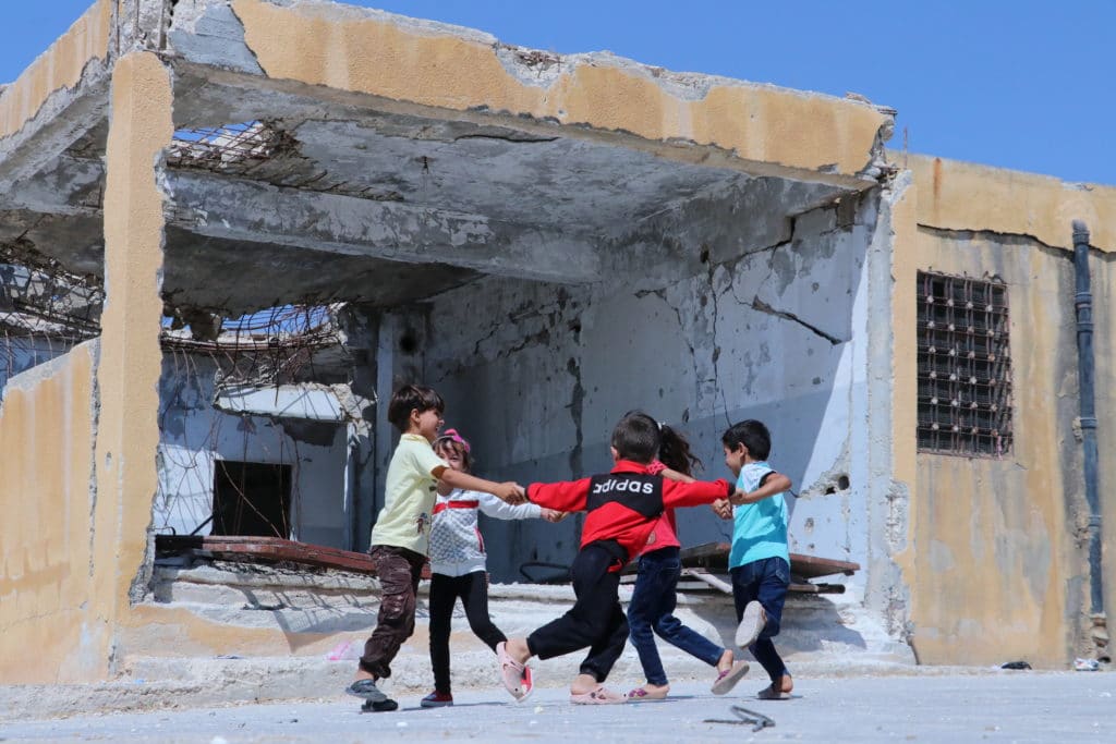 Barn leker utenfor en ødelagt skolebygning.