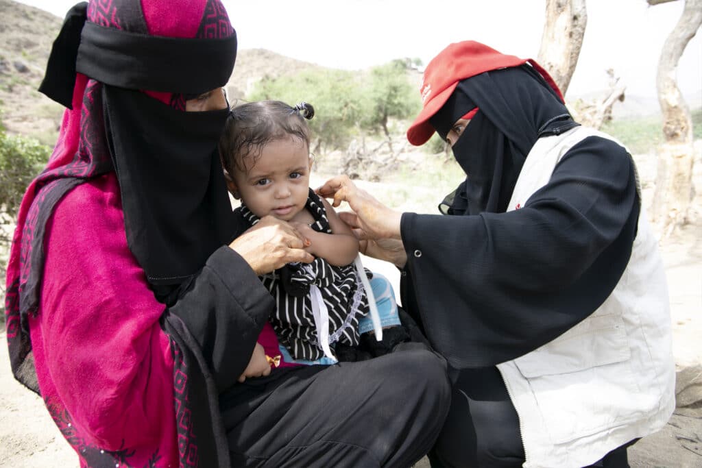 Ei 15 måneder gammel jente sitter på fanget til bestemoren sin mens hun blir sjekket av helsepersonell på en Redd Barna-klinikk i Yemen