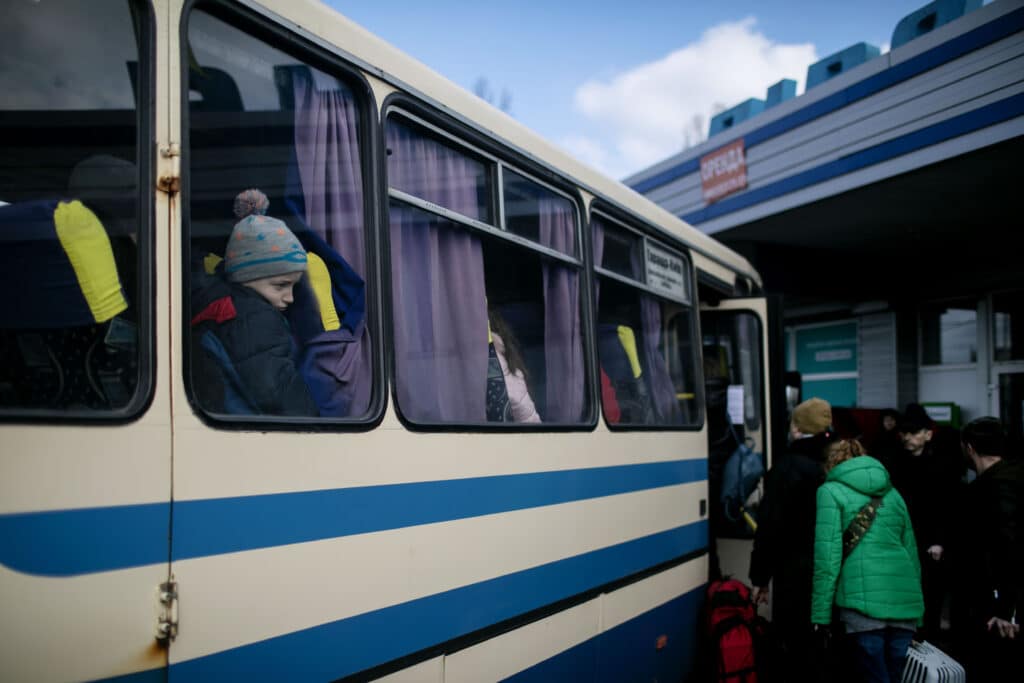 Barn og voksne står i kø for å komme ombord på en buss ut av Kyiv.