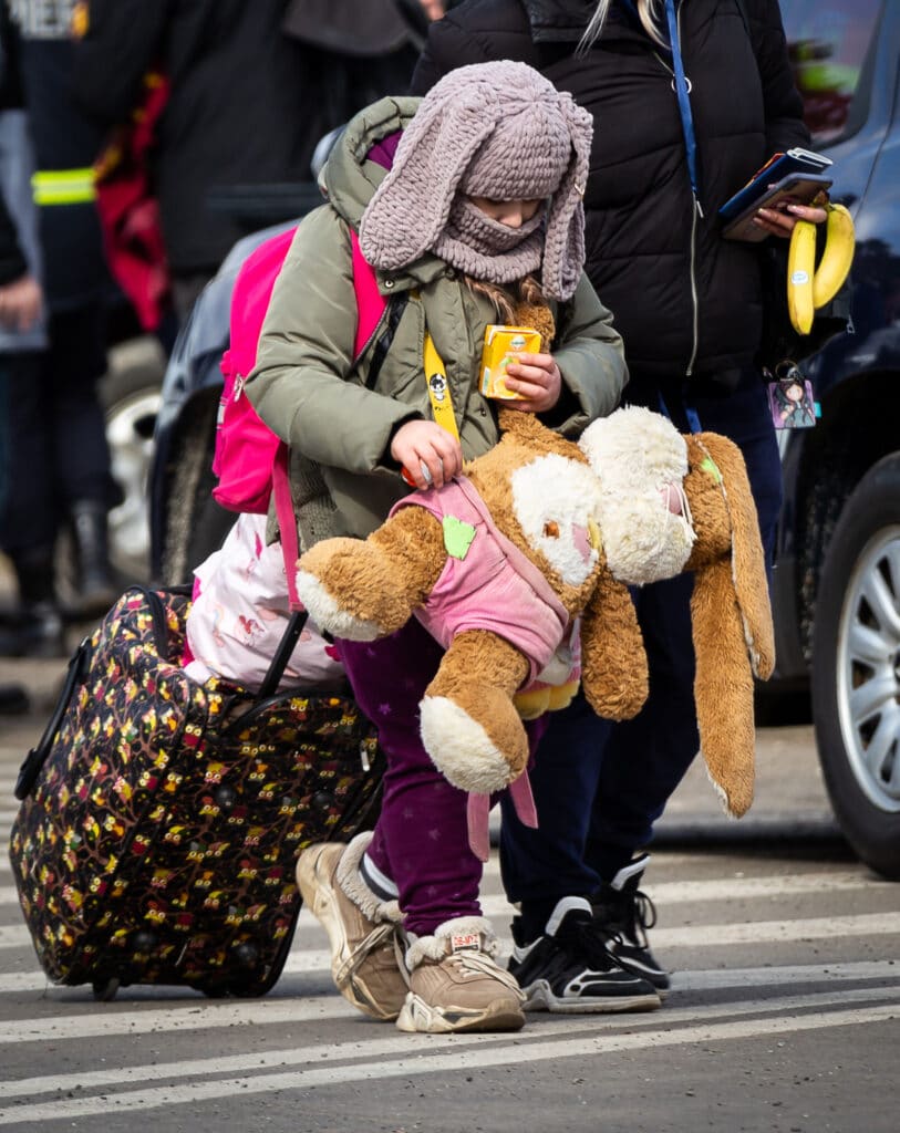 En jente med tjukke vinterklær krysser grensen til Romania mens hun bærer på en ryggsekk og en stor bamse.