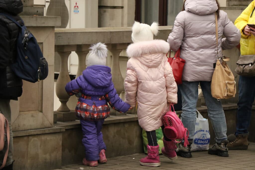 2 barn med tjukke boblejakker står med små ryggsekker - på flukt fra Ukraina