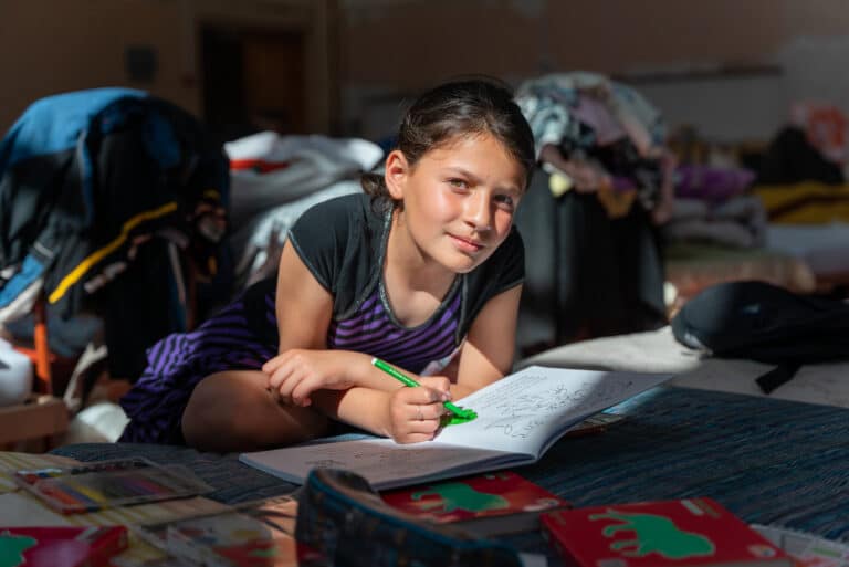 Foto av jente fra Ukraina som fargelegger i en bok. Er på flukt og bor provisorisk på en skole.