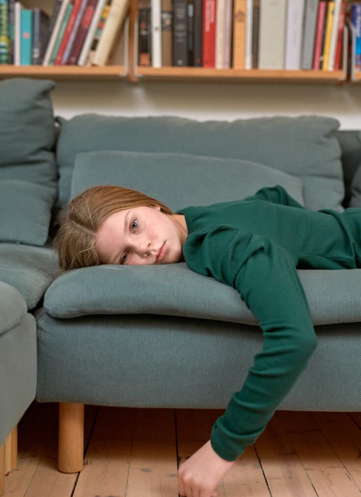 En jente ligger på en sofa og ser tomt inn i kamera