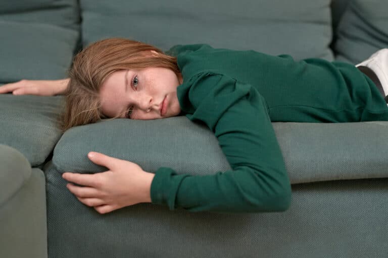 En jente ligger på en sofa og ser tomt inn i kamera