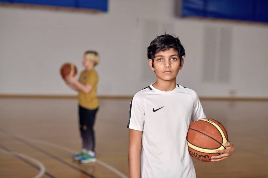 En gutt står i en gymsal, med en basketball i hendene og en alvorlig mine.