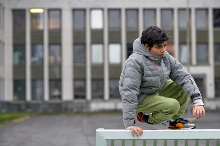 En gutt hopper over et gjerde i en skolegård