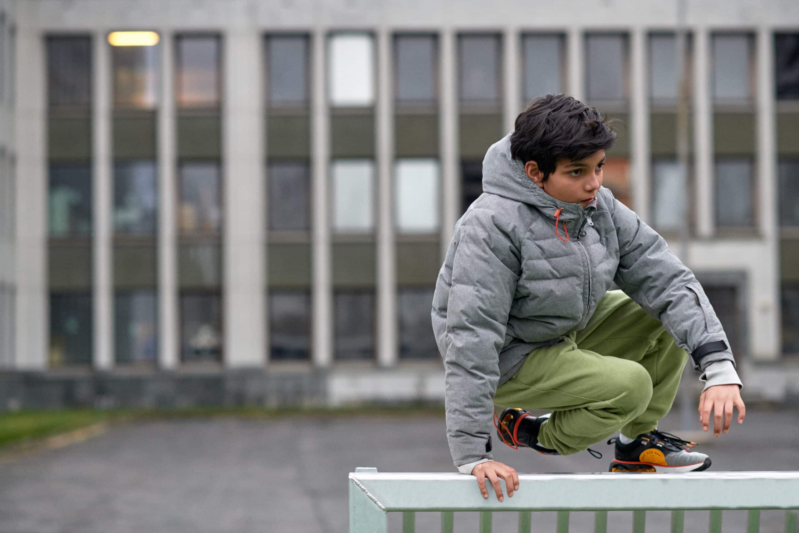 En gutt hopper over et gjerde i en skolegård