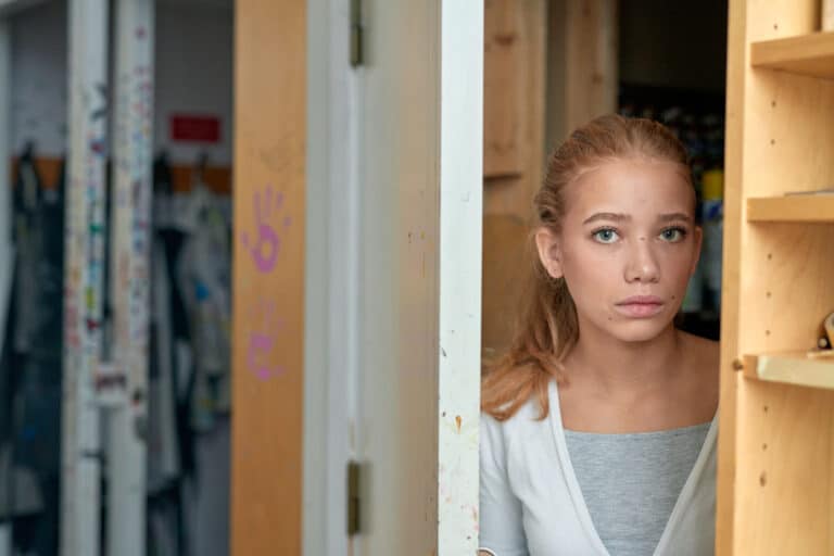 En jente står i en døråpning, ser alvorlig inn i kameraet - få råd og veiledning hvis du er bekymret for et barn