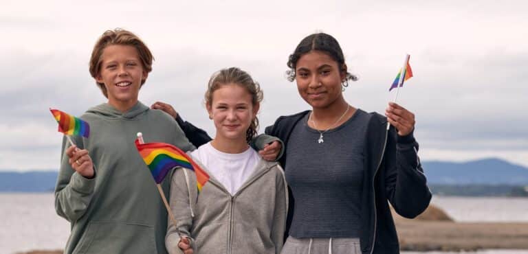 Tre ungdommer har prideflagg og ser inn i kameraet