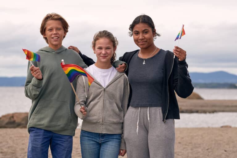Tre ungdommer har prideflagg og ser inn i kameraet