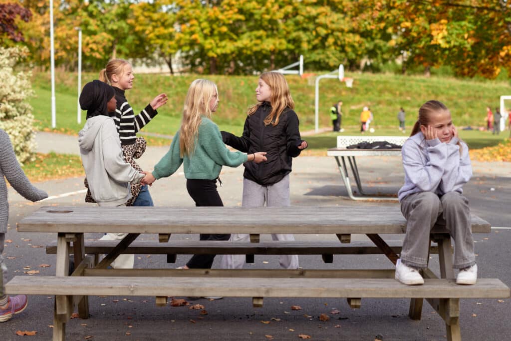 En elev sitter på en benk i skolegården, hun ser lei seg ut