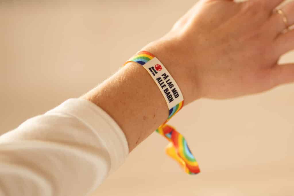 En arm med hvit genser og pride-armbånd på