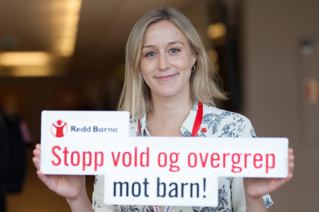 En dame holder en plakat der det står Stopp vold og overgrep mot barn.