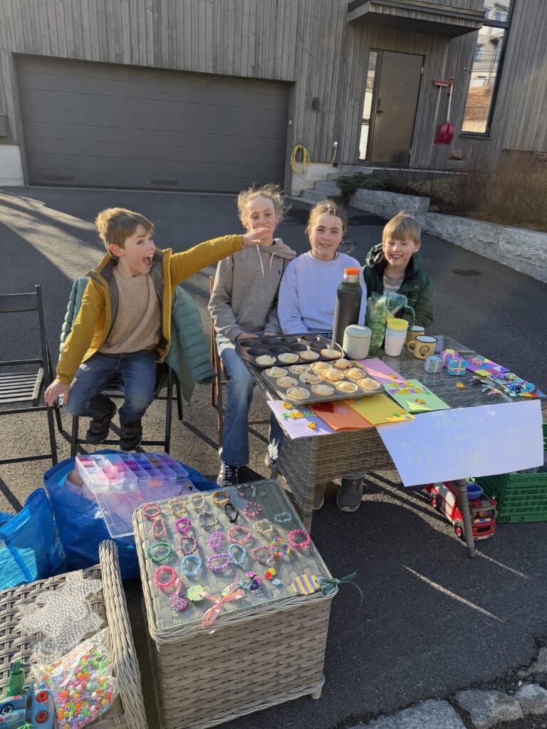 To gutter og to jenter sitter foran bord med muffins, perler, kopper og armbånd