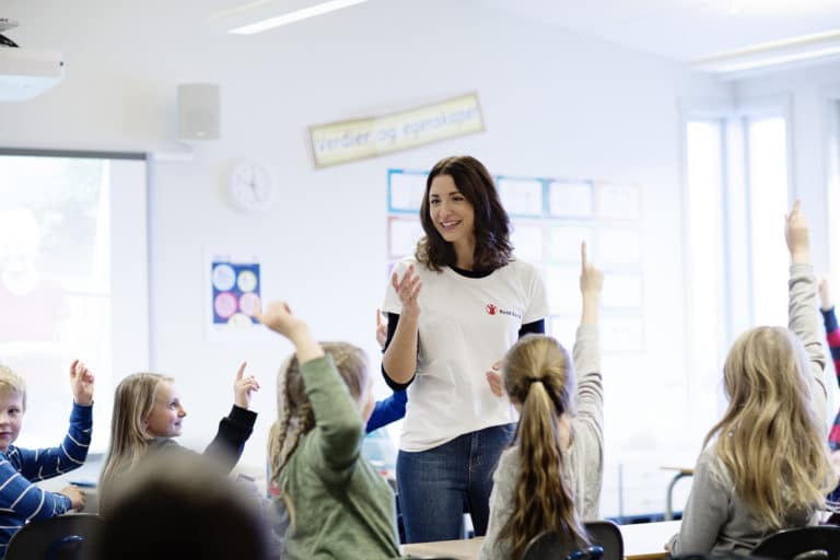 Lærer i klasserom med elever som rekker omm hendene