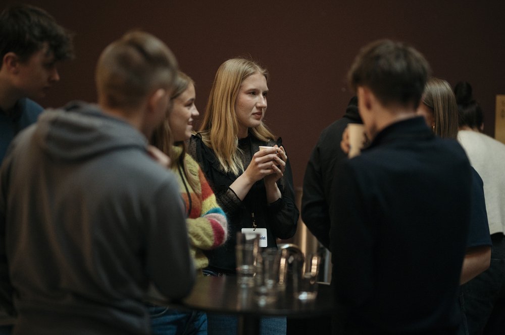 En gjeng mennesker står flokket sammen rundt et lite bord og diskuterer