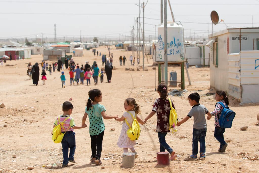 en rekke med syriske barn som går hånd i hånd i en flyktningeleir i Jordan