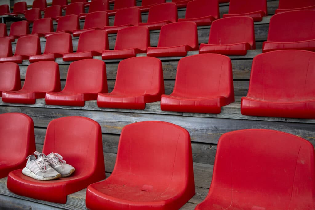 Et par forlatte joggesko står igjen på en helt tom tribune med røde seter