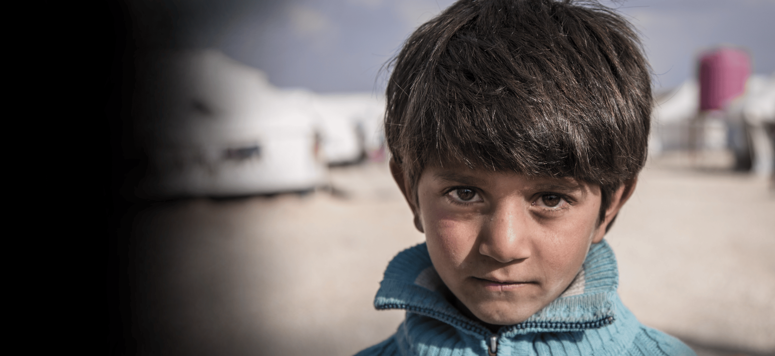 Syrisk gutt med blå genser ser inn i kameraet