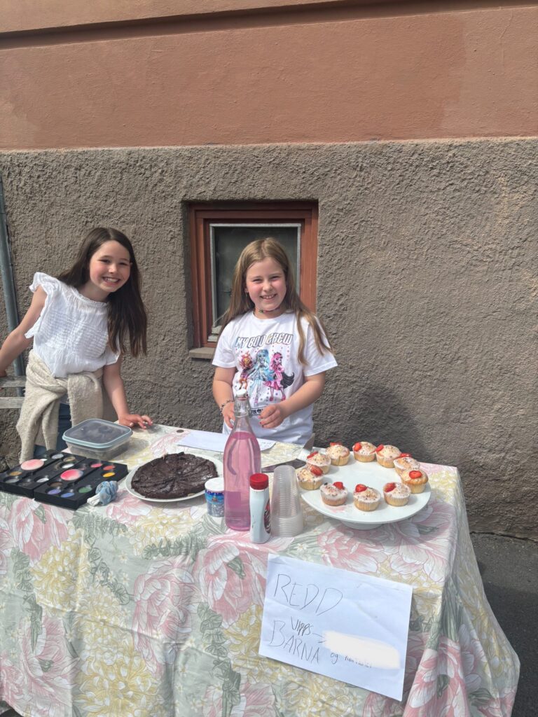 To jenter holder basar der de selger muffins, brownies og ansiksmaling.