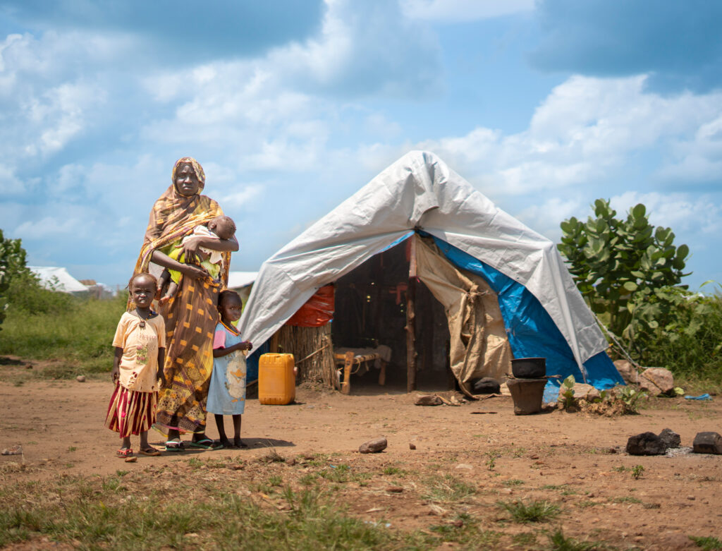 En mor med 3 små barn står utenfor teltet sitt i en leir for internt fordrevne i Sudan
