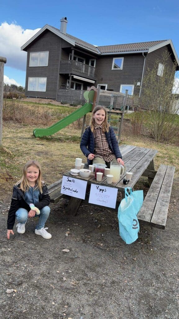 To jenter viser frem basaren sin uten for et hus