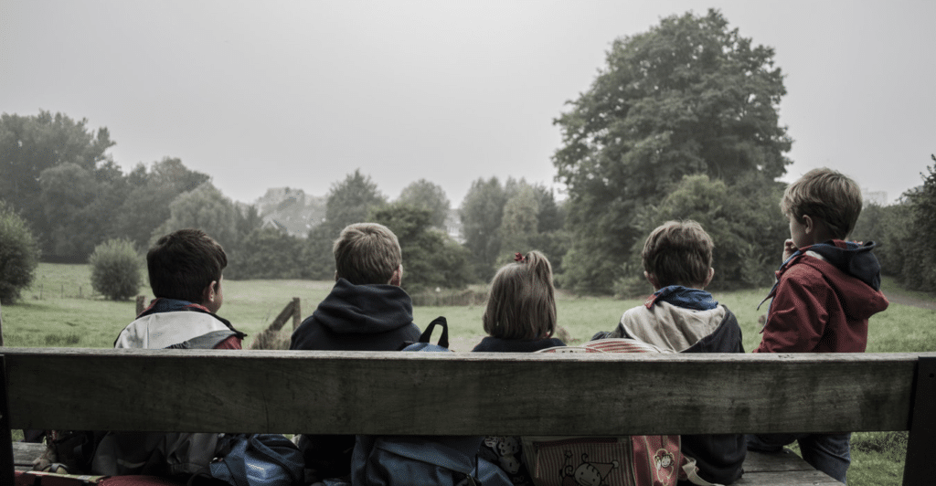 5 Barn som sitter med ryggen til på en benk i skogen.