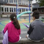 To barn sitter med ryggen til på en lekeplass utenfor et asylmottak.