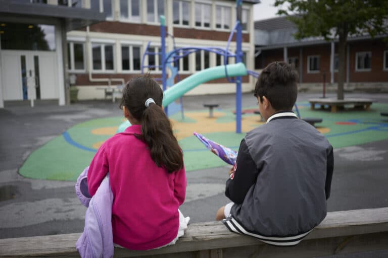 To barn sitter med ryggen til på en lekeplass utenfor et asylmottak.