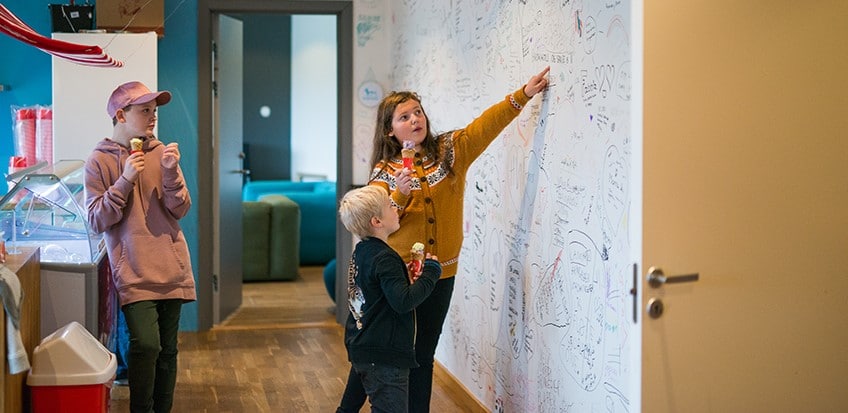 Bilde av tre barn som peker på en påskrevet vegg hos Stine Sofie Stiftelsen