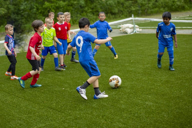 En gjeng med unge gutter spiller fotball i fotballdraker på en gressbane.