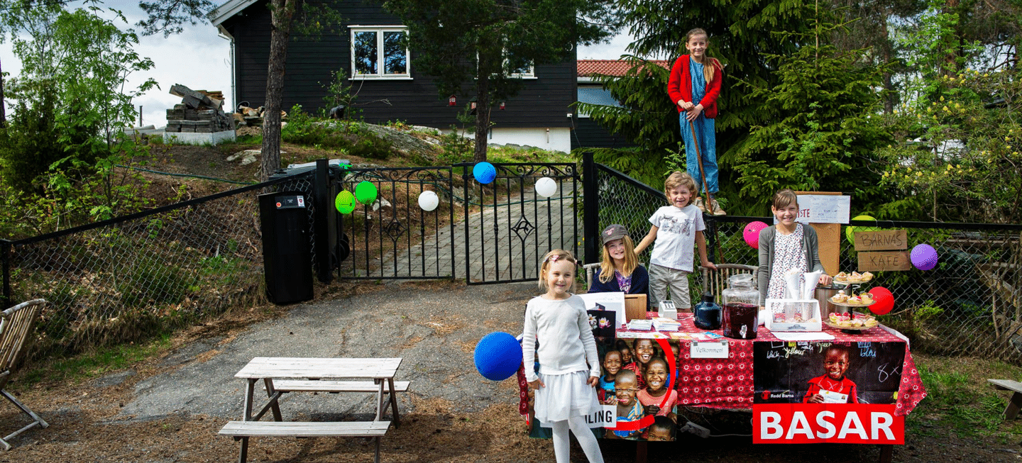 En gruppe barn holder basar utenfor huset sitt, med plakater og ballonger
