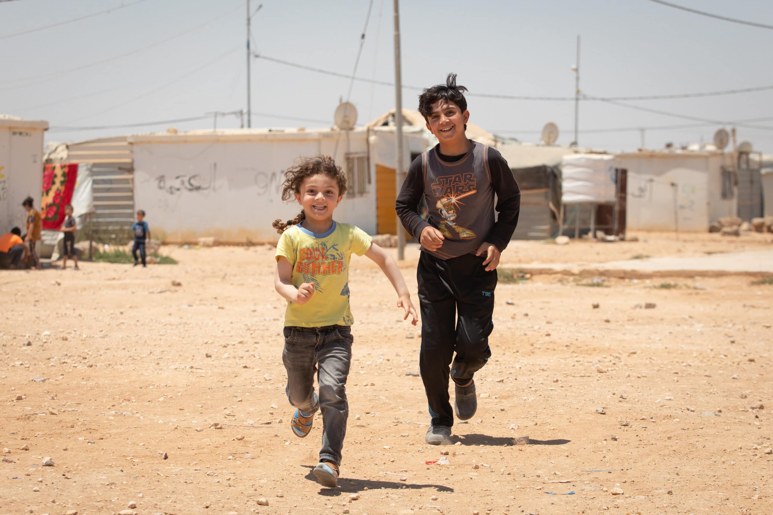 2 gutter løper mot kameraet i en flyktningleir