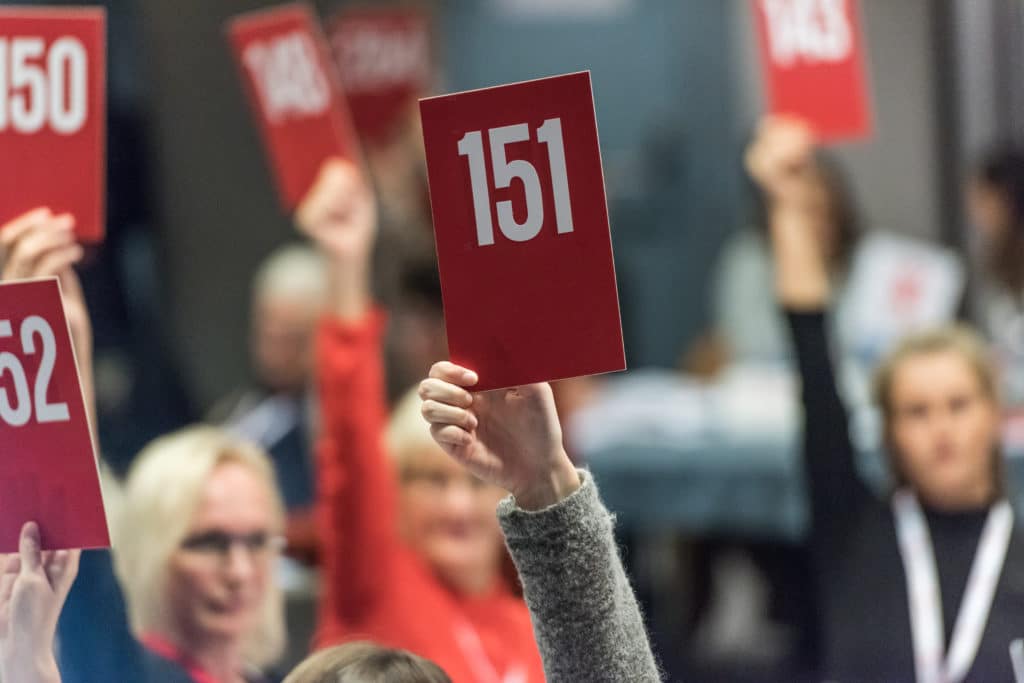 Mange hender holder opp røde stemmekort.