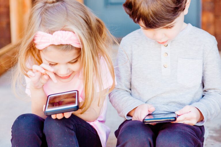 Liten jente og liten gutt sitter ved siden av hverandre og ser på hver sin mobiltelefon