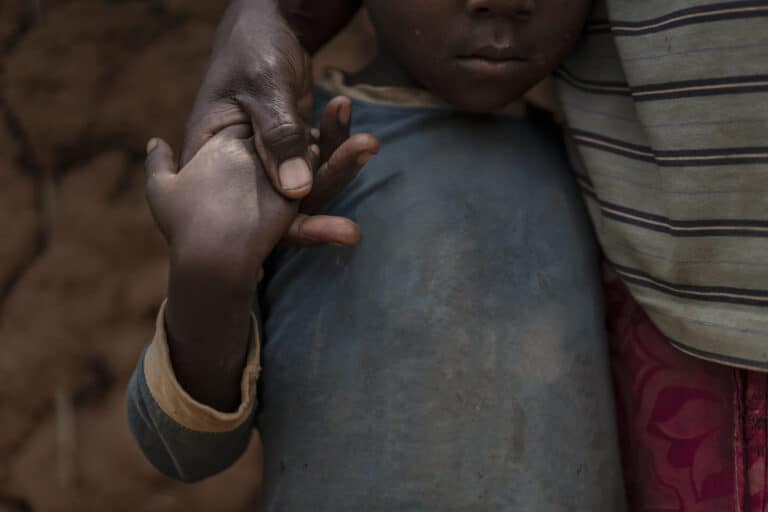 Et barn står og holder i hånden til moren sin. Vi ser ikke ansiktene.