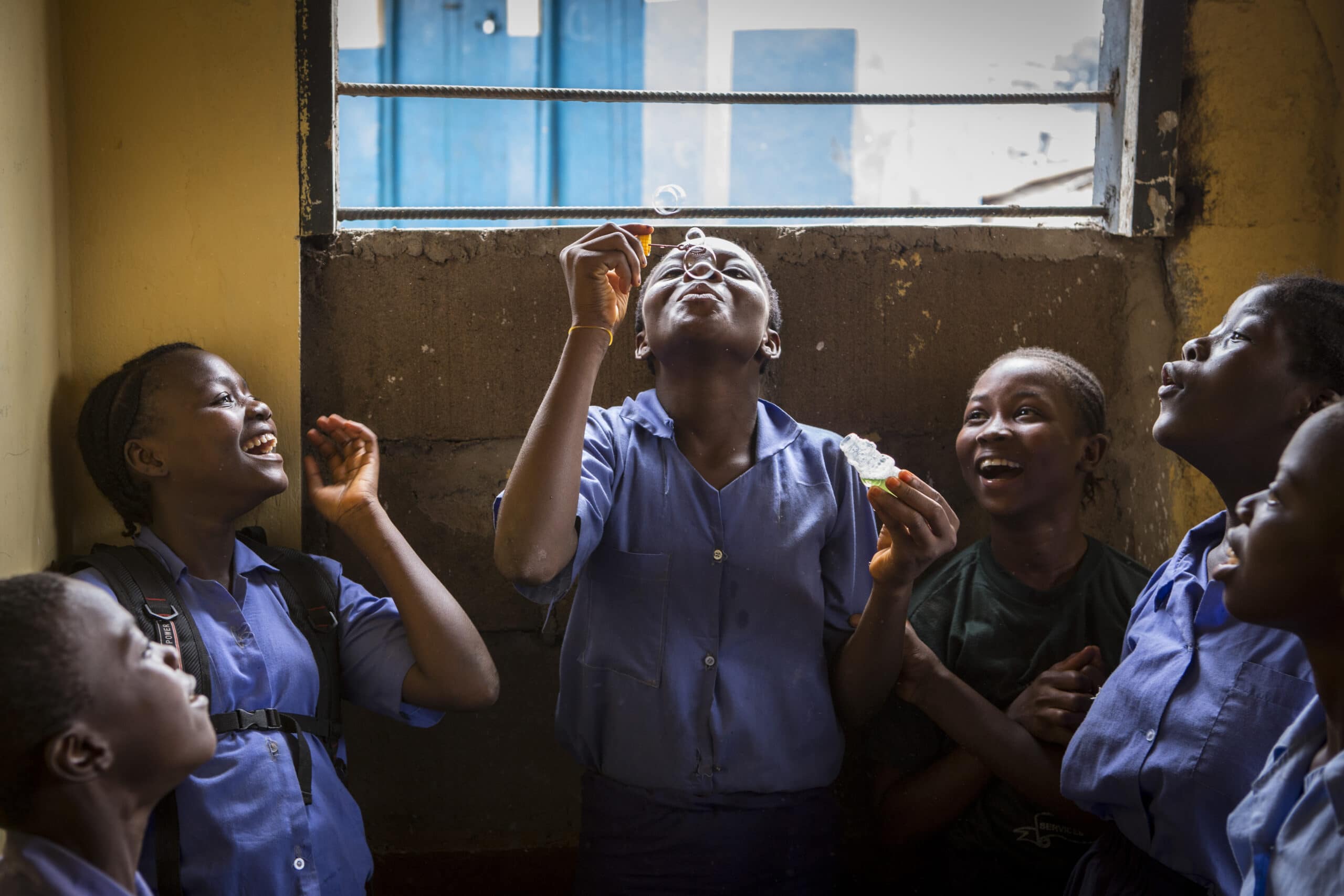 En gruppe barn i blå skoleuniformer ser på et barn som blåser såpebobler opp i luften.