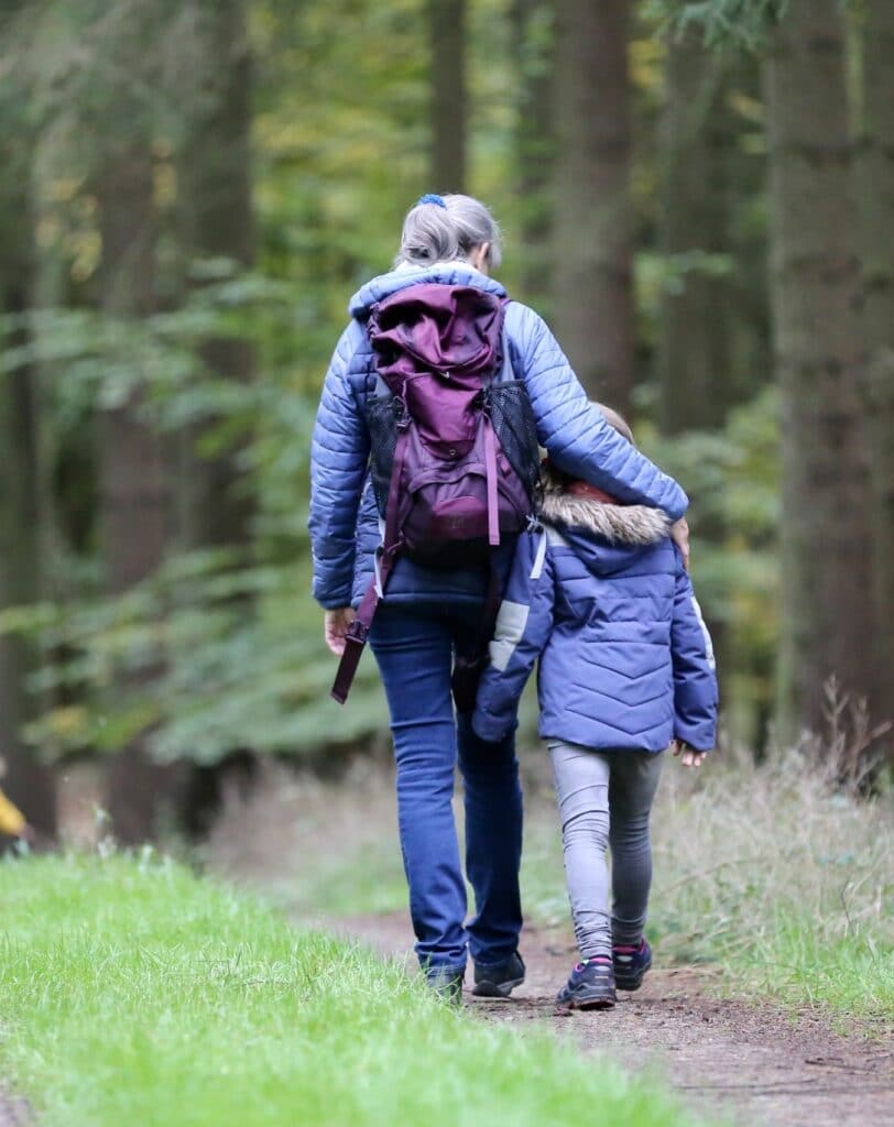 En voksen og et barn går på en tur langs en skogssti. i bakgrunnen er det flere barn.