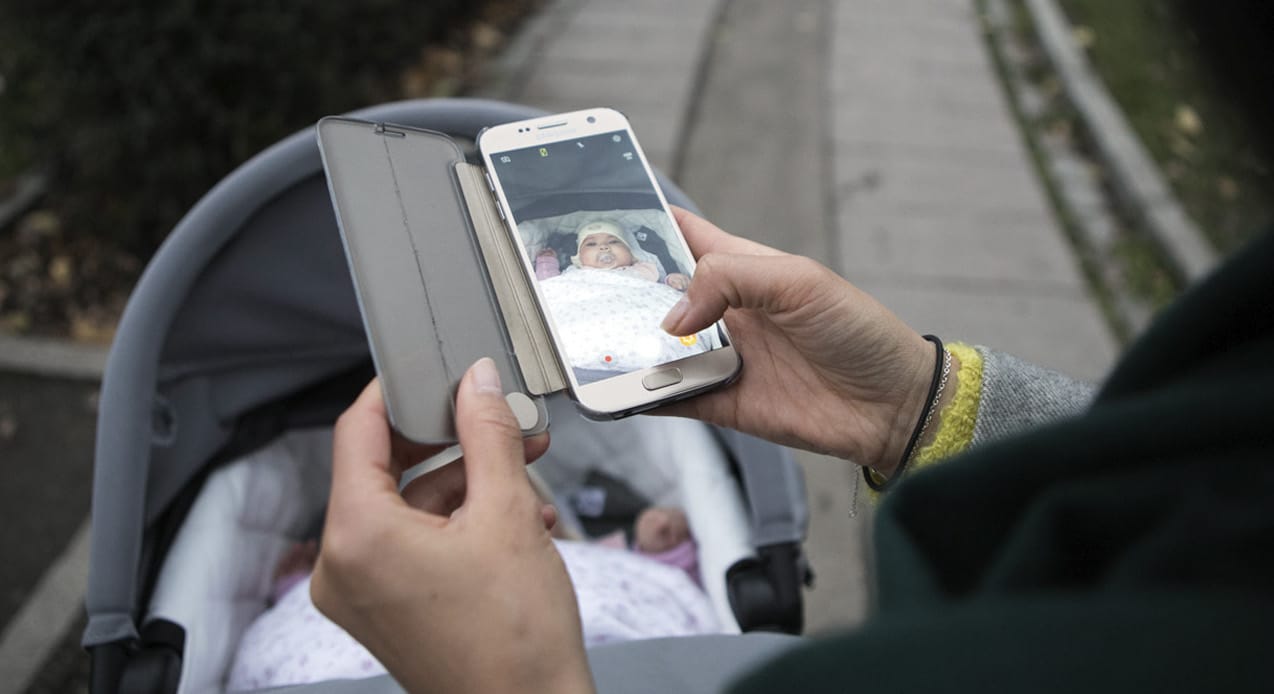 En mor som tar bilde med mobilen sin av et barn i en barnevogn