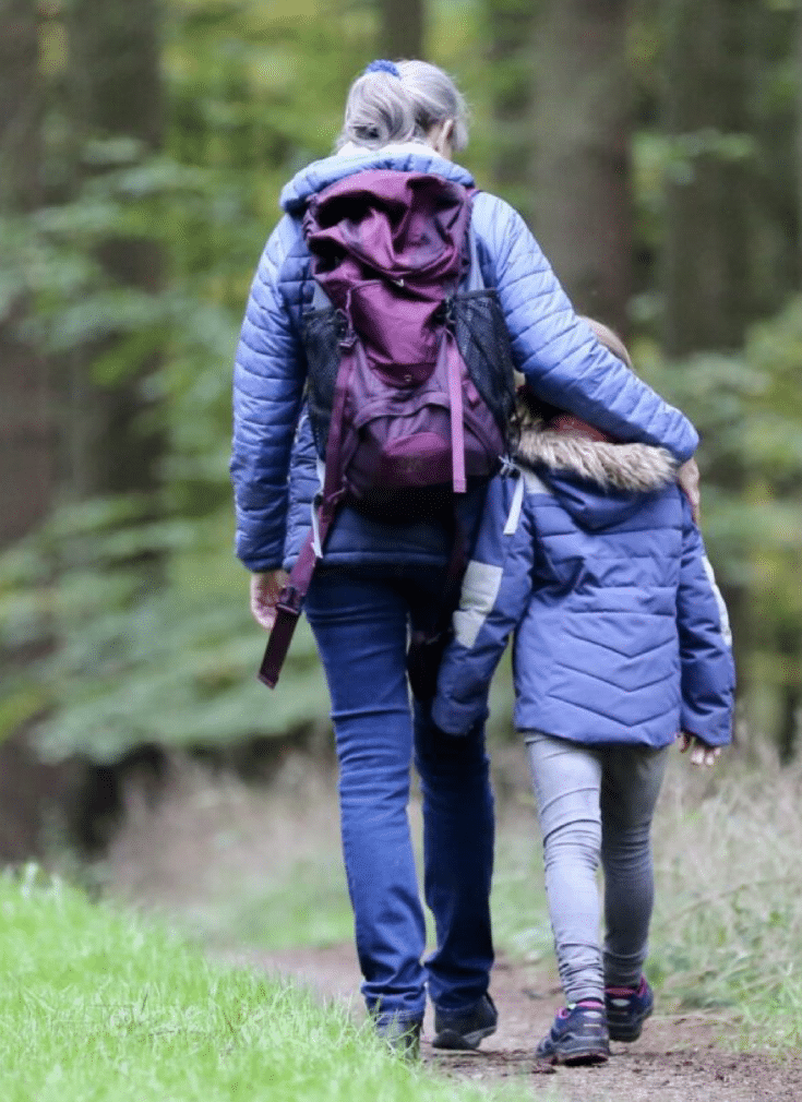 En voksen og et barn går sammen på en skogsvei. Den voksne holder armen vennlig på skulderen til barnet.